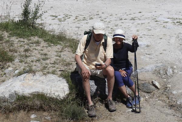 Two hikers are taking a break on a sunny day, sitting on rocks along a dusty trail